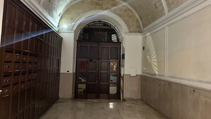A corridor with a vaulted ceiling, a large wooden door with multiple compartments, and a tiled floor.