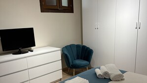 A bedroom with a bed, a TV on a dresser, a chair, and a wardrobe.