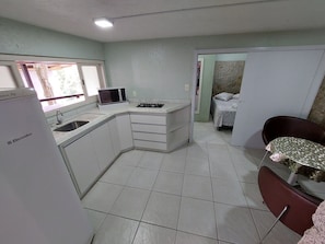 A compact kitchen with a refrigerator, microwave, sink, and a small dining area with a table and chair. - Loft Barra da Fortaleza - Piscina (Florianópolis)