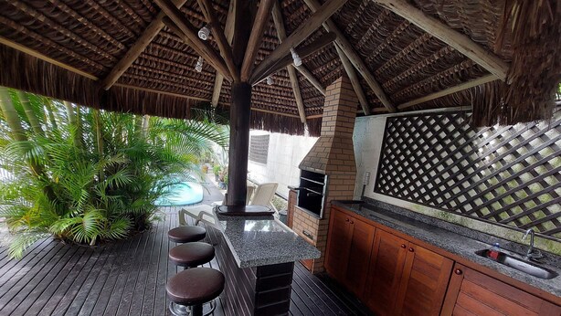 An outdoor kitchen area with a brick oven, bar stools, and a pool. - Loft Barra da Fortaleza - Piscina (Florianópolis)