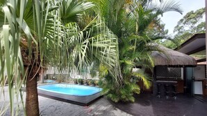 A pool area with a hot tub, surrounded by lush tropical plants and a thatched-roof structure. - Loft Barra da Fortaleza - Piscina (Florianópolis)