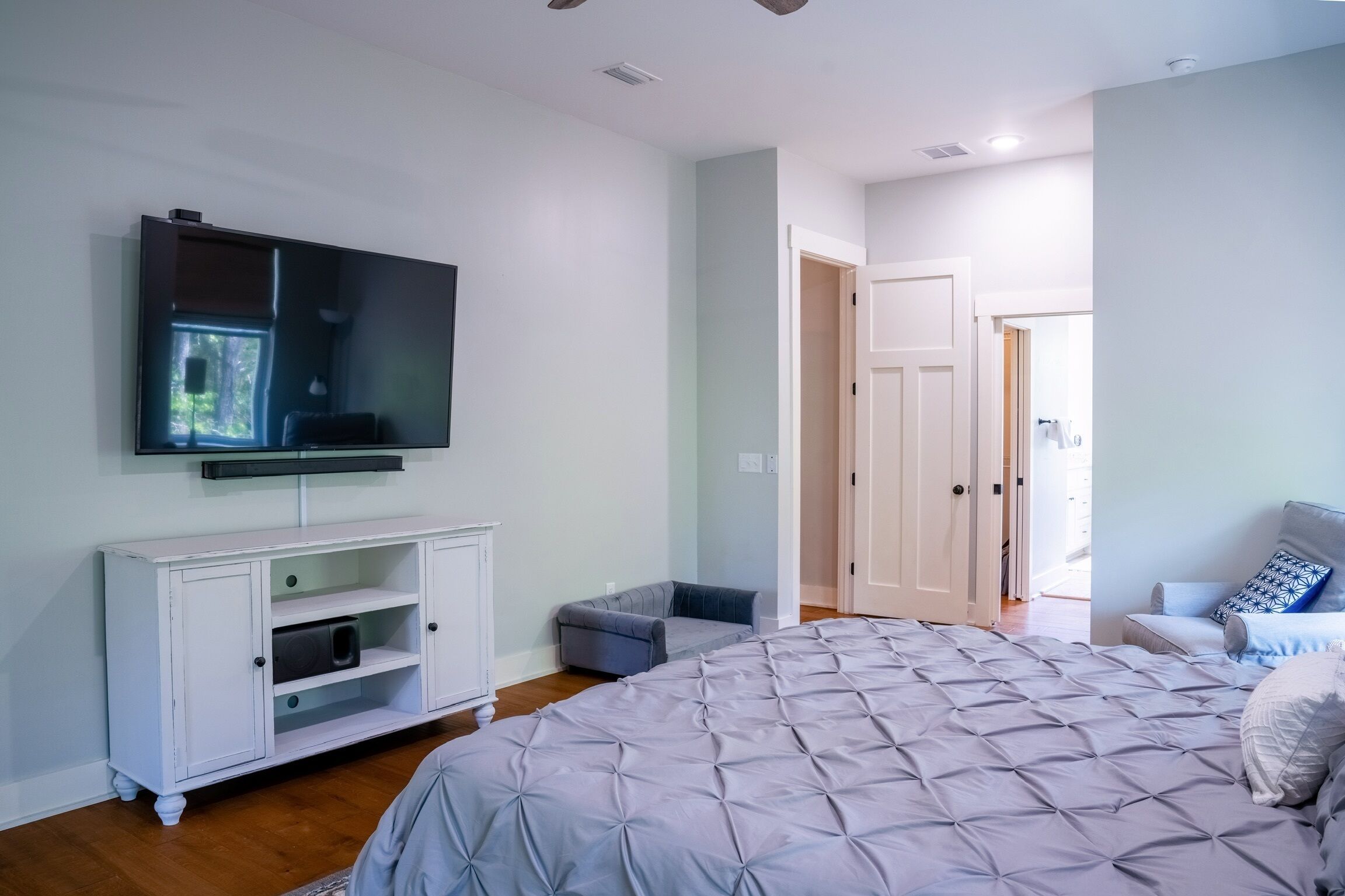 A bedroom with a large bed, a TV mounted on the wall, a white cabinet, and a door leading to another room.