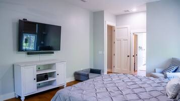 A bedroom with a large bed, a TV mounted on the wall, a white cabinet, and a door leading to another room.
