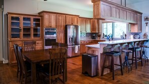A kitchen with wooden cabinets, stainless steel appliances, a dining table with chairs, and a bar area with stools. - NEW LISTING ★ WATERFRONT ★ FIREPIT (Vernon)