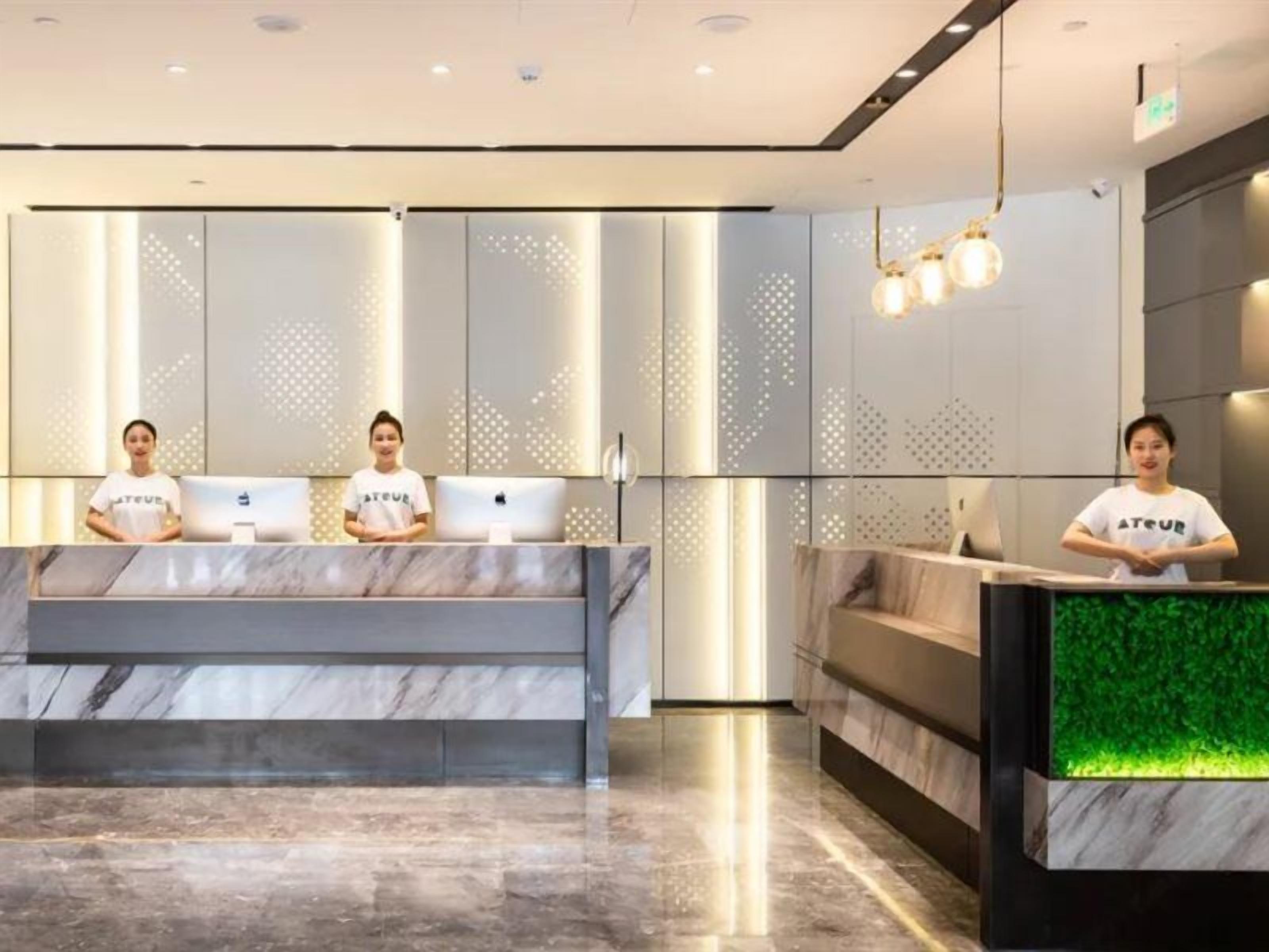A hotel reception area with a marble counter, a green illuminated display, and a seating area.