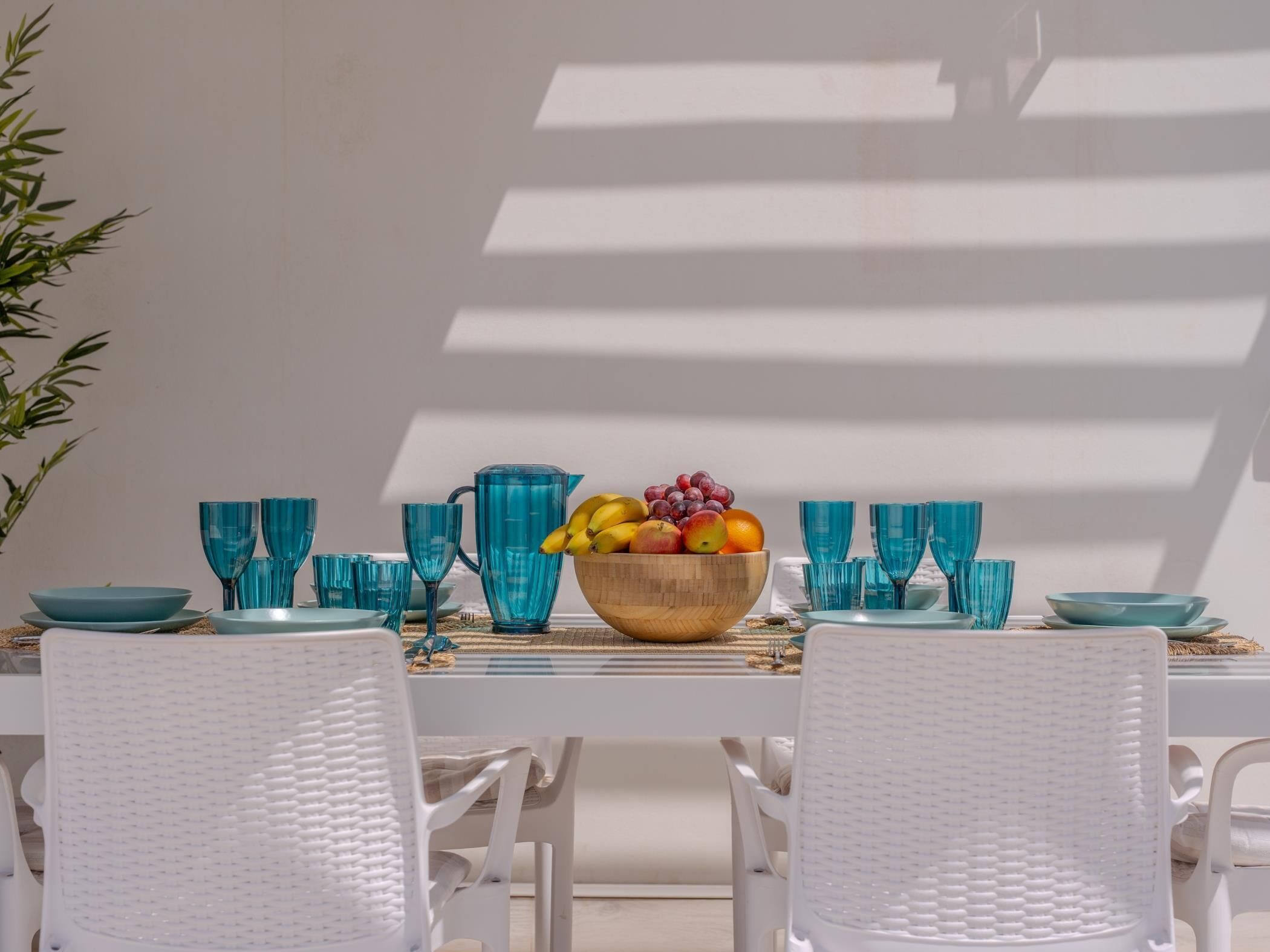 Een tafel gedekt met blauw glaswerk, een houten schaal met fruit en witte stoelen.
