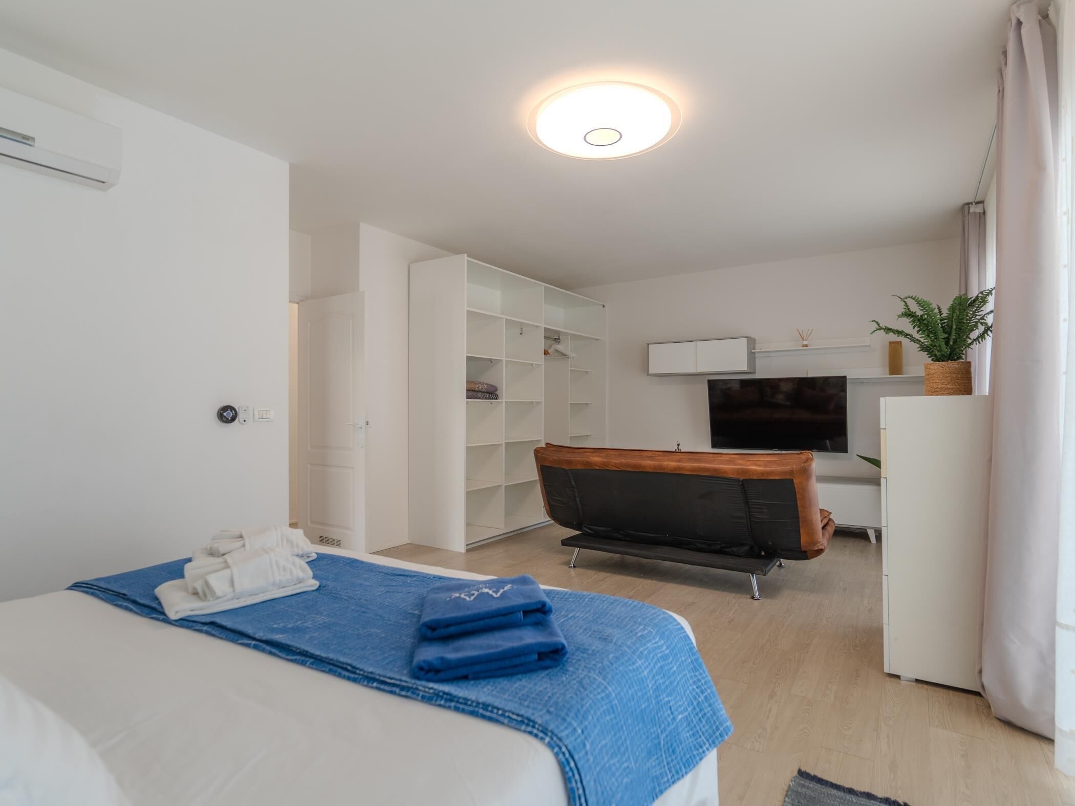 A modern hotel room with a bed, a desk, a chair, a TV, and a wardrobe.