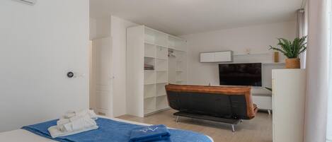 A modern hotel room with a bed, a desk, a chair, a TV, and a wardrobe.