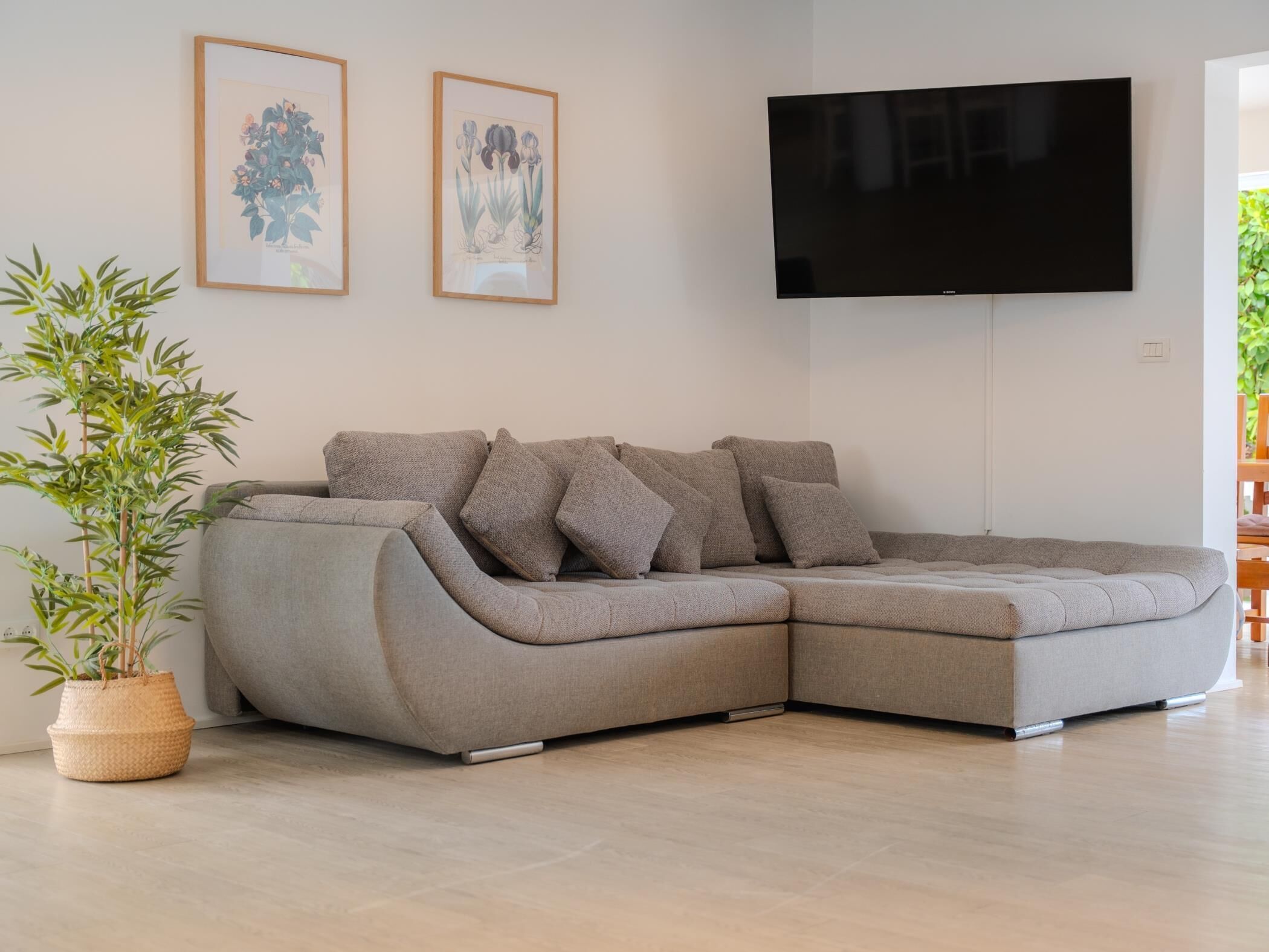 A modern living room with a sectional sofa, a flat-screen TV, and two framed botanical prints on the wall.
