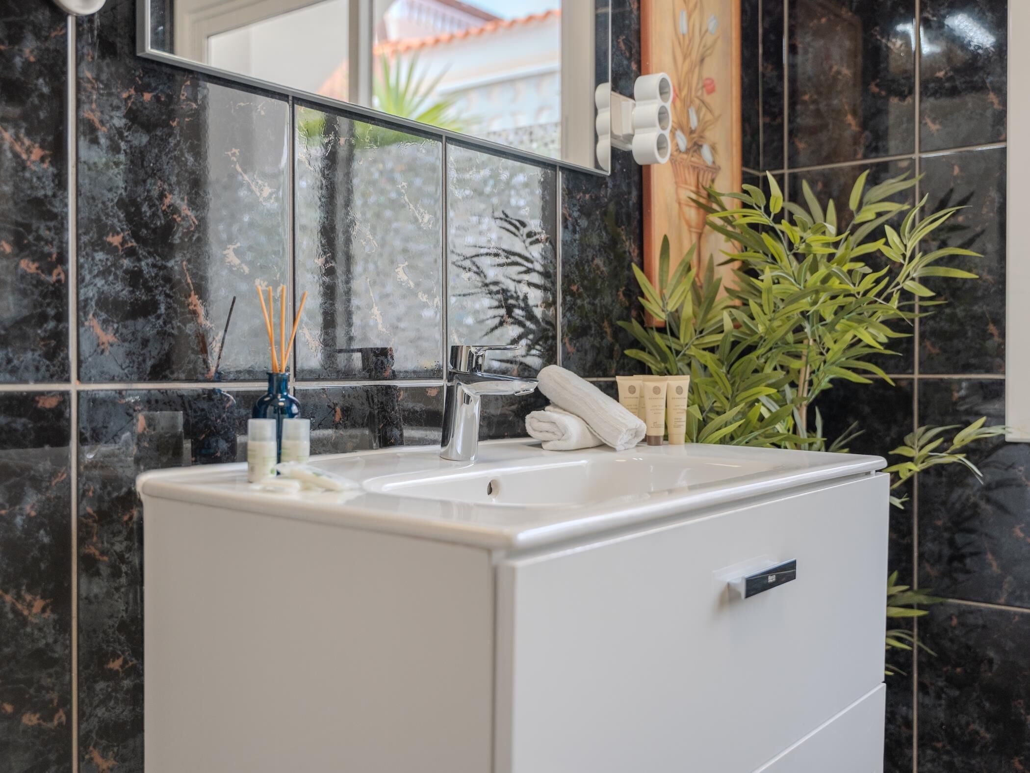 Un baño con lavamanos blanco, espejo y planta en maceta.