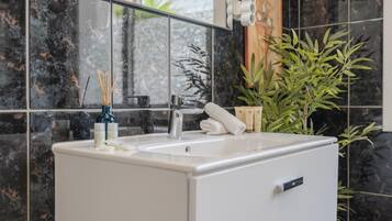Un baño con lavamanos blanco, espejo y planta en maceta.