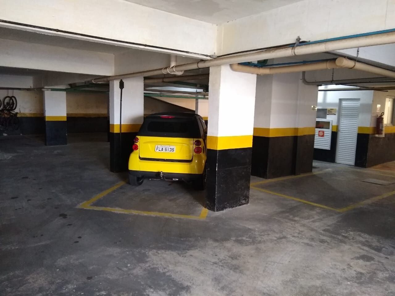 Un aparcamiento con un coche amarillo estacionado bajo un pilar.