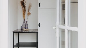 Un couloir avec une porte blanche, une étagère en métal noir et un vase contenant des plantes séchées.