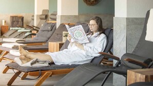 Un espace de détente avec des fauteuils inclinables, une personne lisant un livre et un banc en bois.