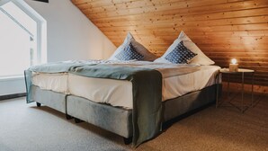 Une chambre avec un plafond en bois, un lit recouvert de plusieurs coussins, une table de chevet avec une bougie et une fenêtre laissant entrer la lumière naturelle.