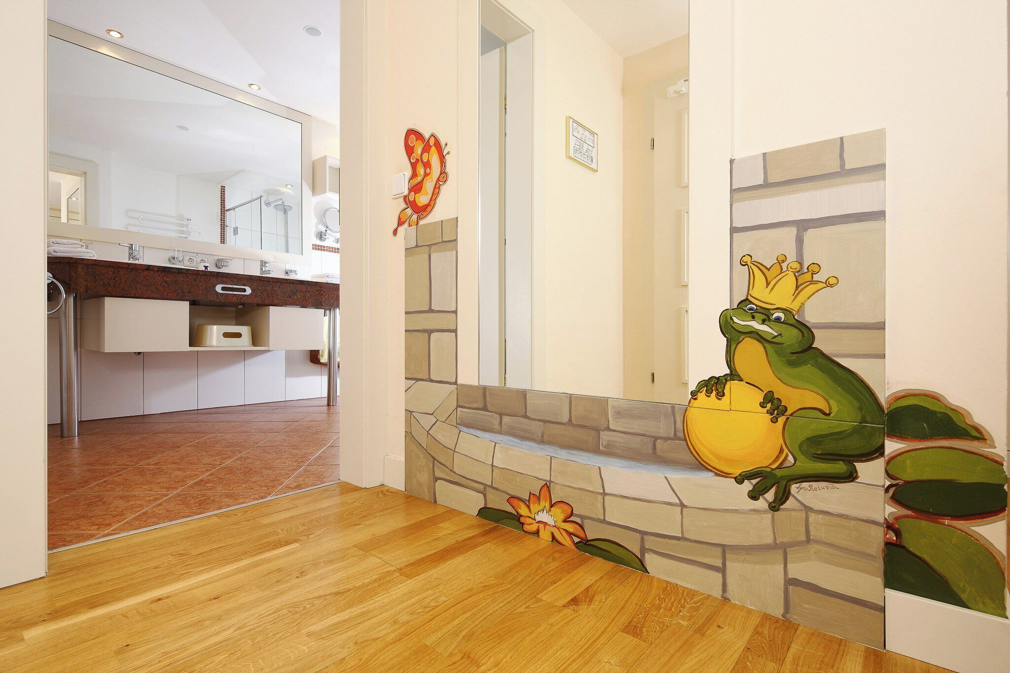 A modern kitchen with a wooden floor, a stone wall, and a frog mural.