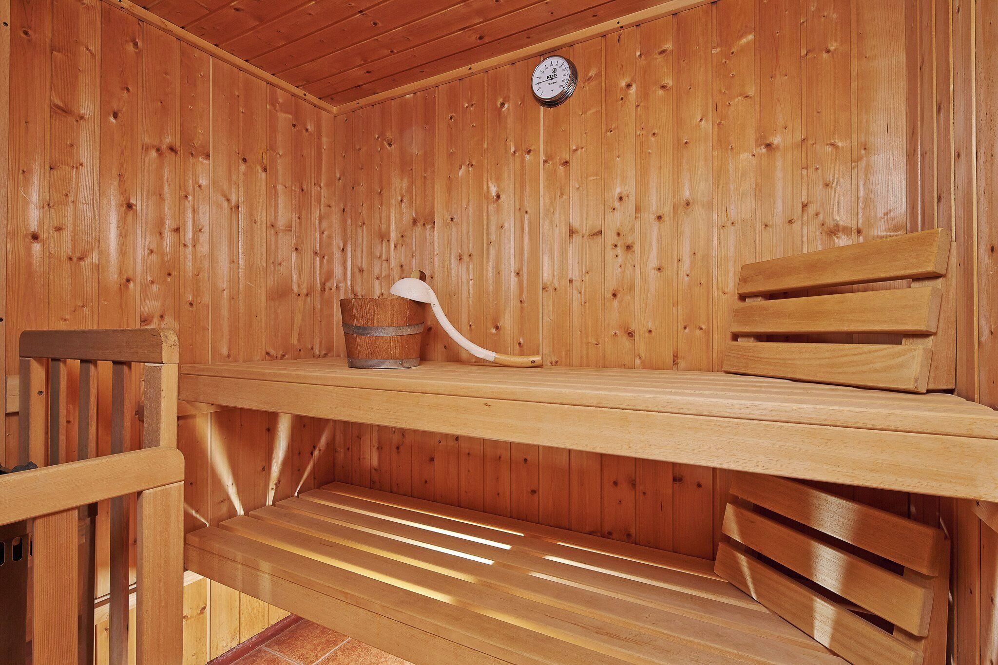 A wooden sauna with a bench, a bucket, and a clock on the wall.