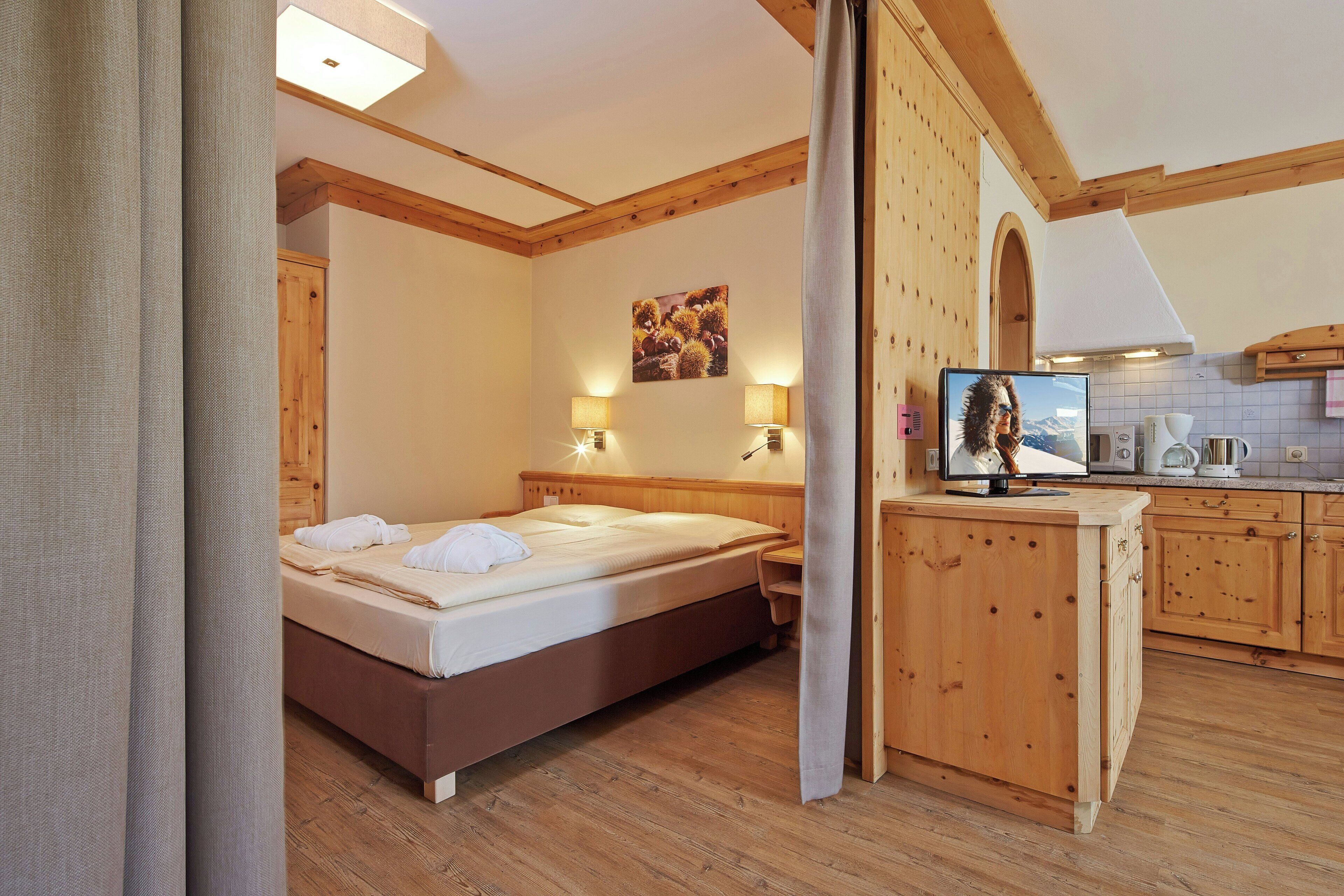 Habitació d'hotel amb llit de fusta, escriptori i petita cuina.