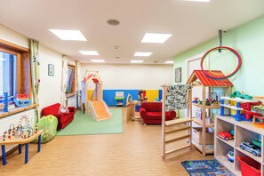 A children's playroom with a slide, play tables, and a toy car display. - Das Hopfgarten Aparthotel (Hopfgarten im Brixental)