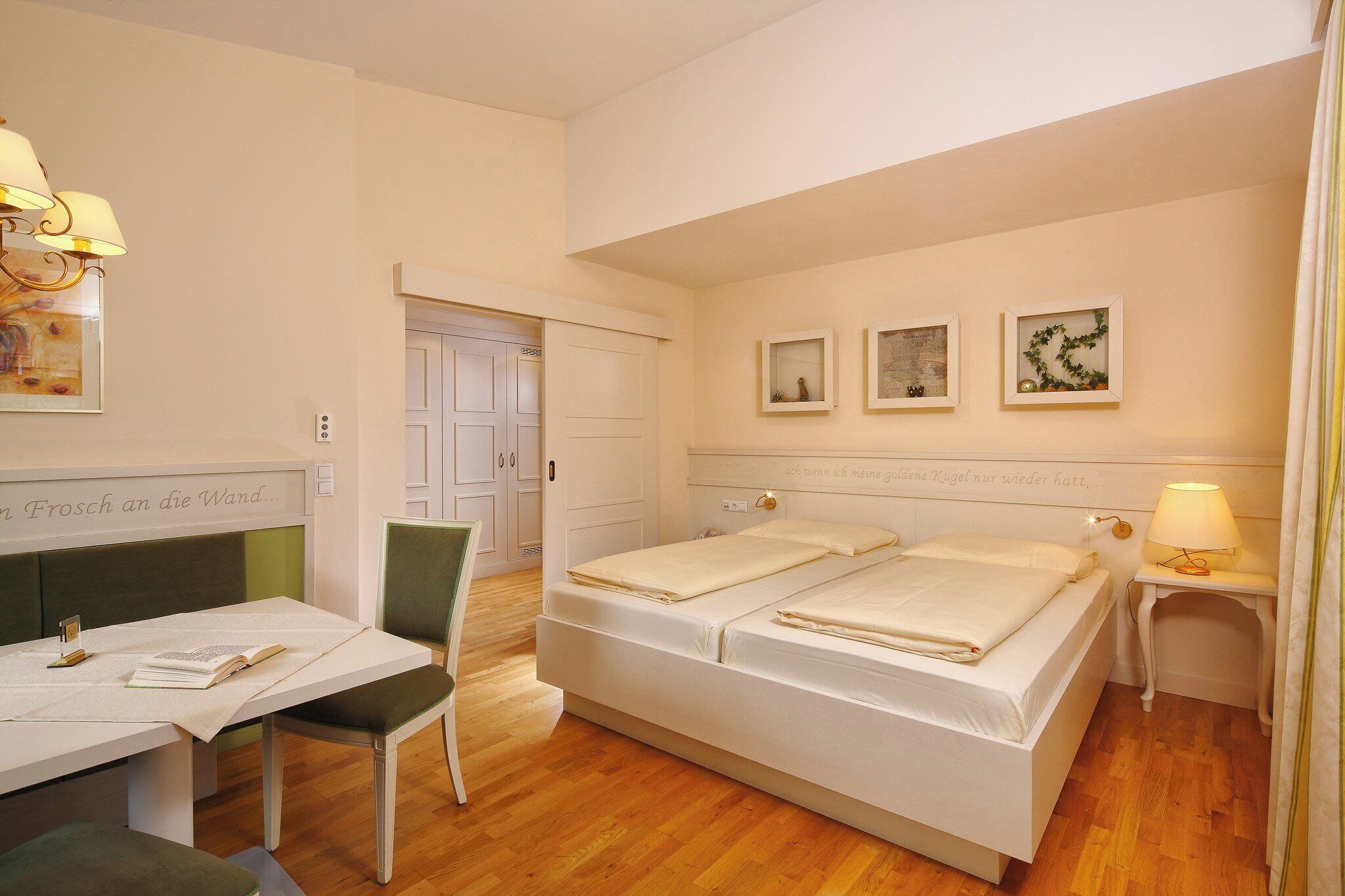 Quarto de hotel com uma cama, uma escrivaninha, uma cadeira e uma pequena mesa.