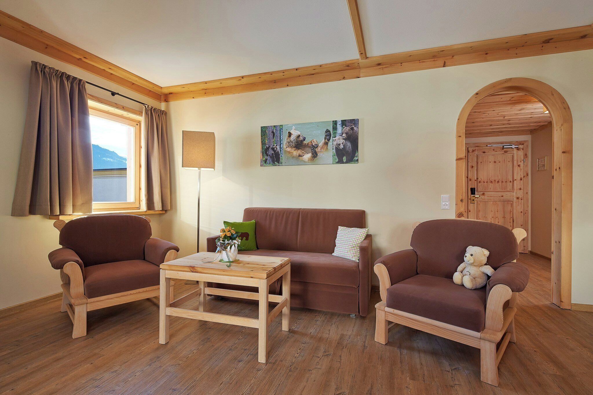 Ein Zimmer mit Holzmöbeln, einer Couch, zwei Sesseln, einem Couchtisch und einem Gemälde an der Wand.