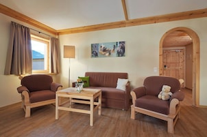 Una habitación con muebles de madera, un sofá, dos sillones, una mesa de centro y un cuadro en la pared.