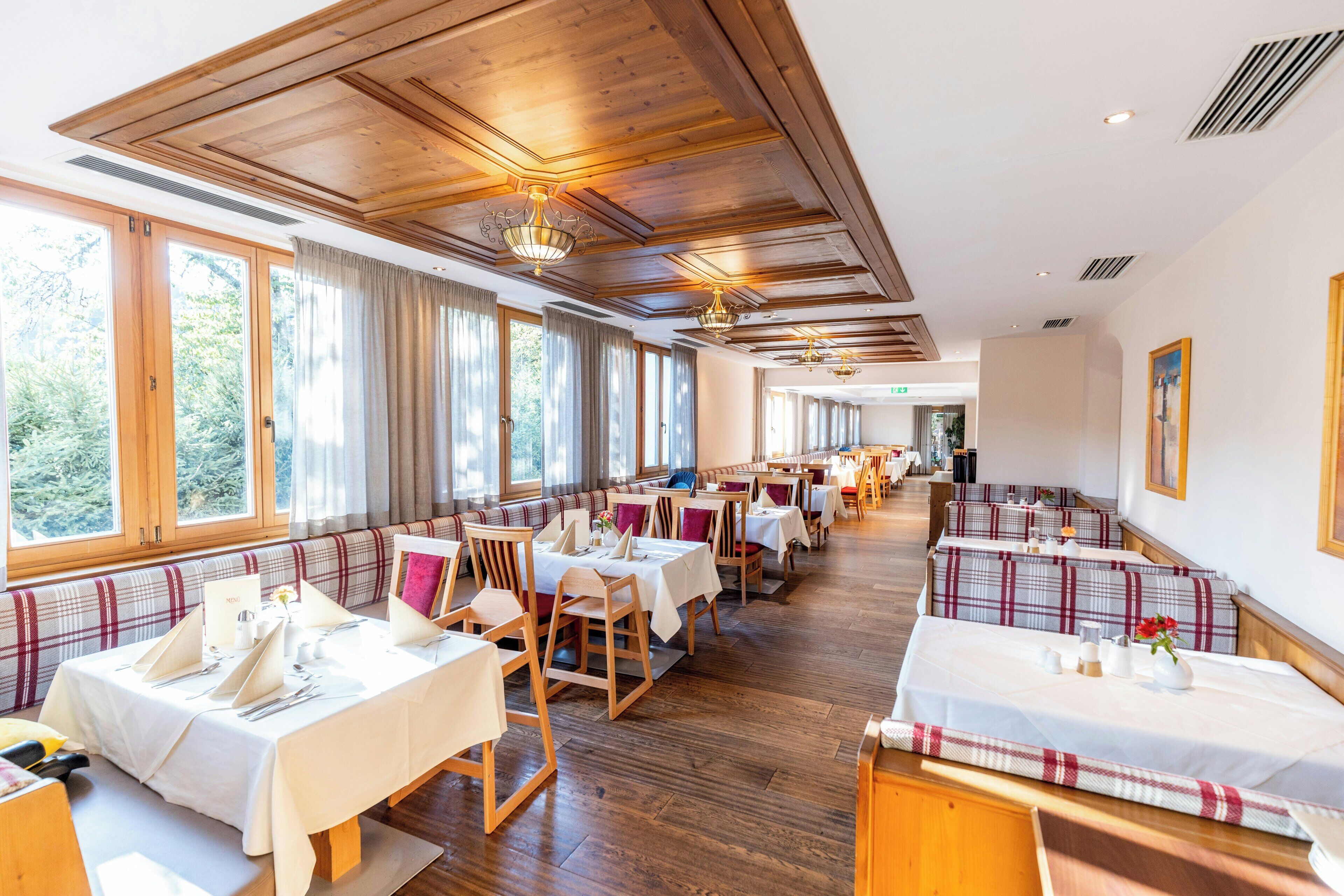 Un restaurant avec des planchers en bois, des tables recouvertes de nappes blanches et des bancs avec des coussins à carreaux.