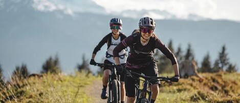 Deux cyclistes sur un sentier de montagne, avec un ciel dégagé et des montagnes à l’horizon.
