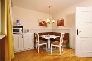 A compact kitchen with a dining area, featuring a microwave, a kettle, and a table with chairs. - Das Hopfgarten Aparthotel (Hopfgarten im Brixental)