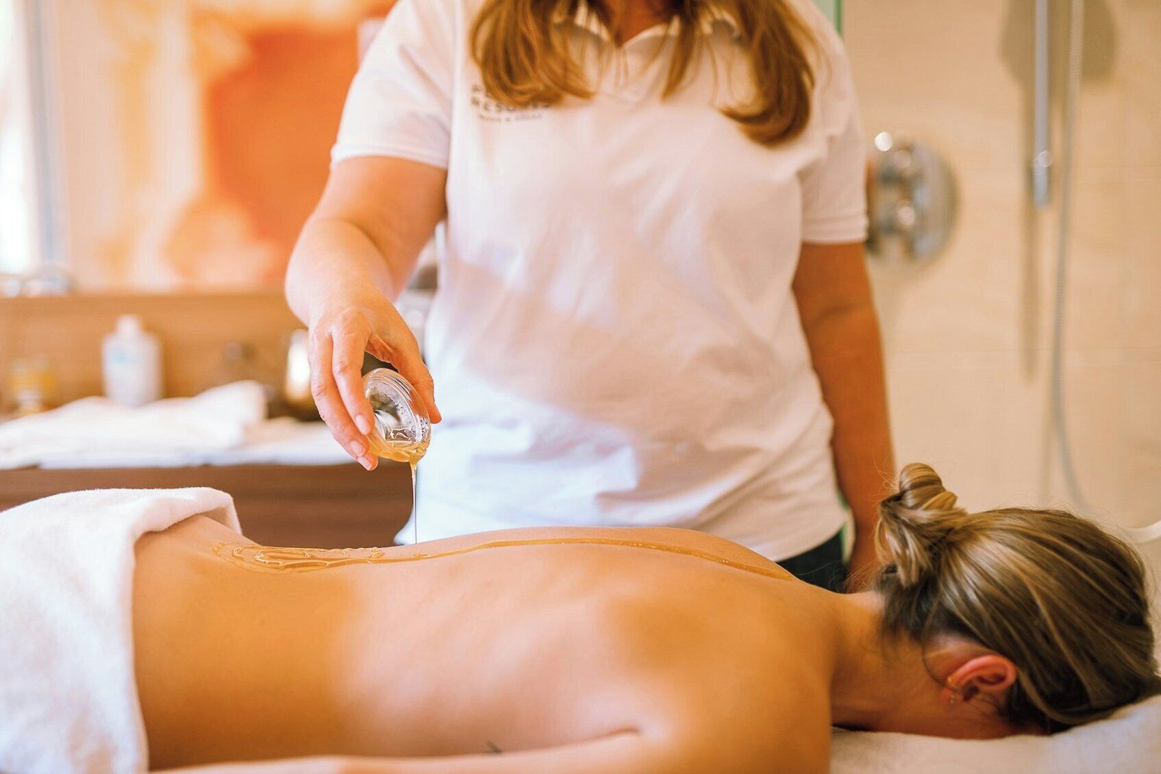 Een persoon ontvangt een massage in een kamer met een houten vloer en een handdoek op het bed.