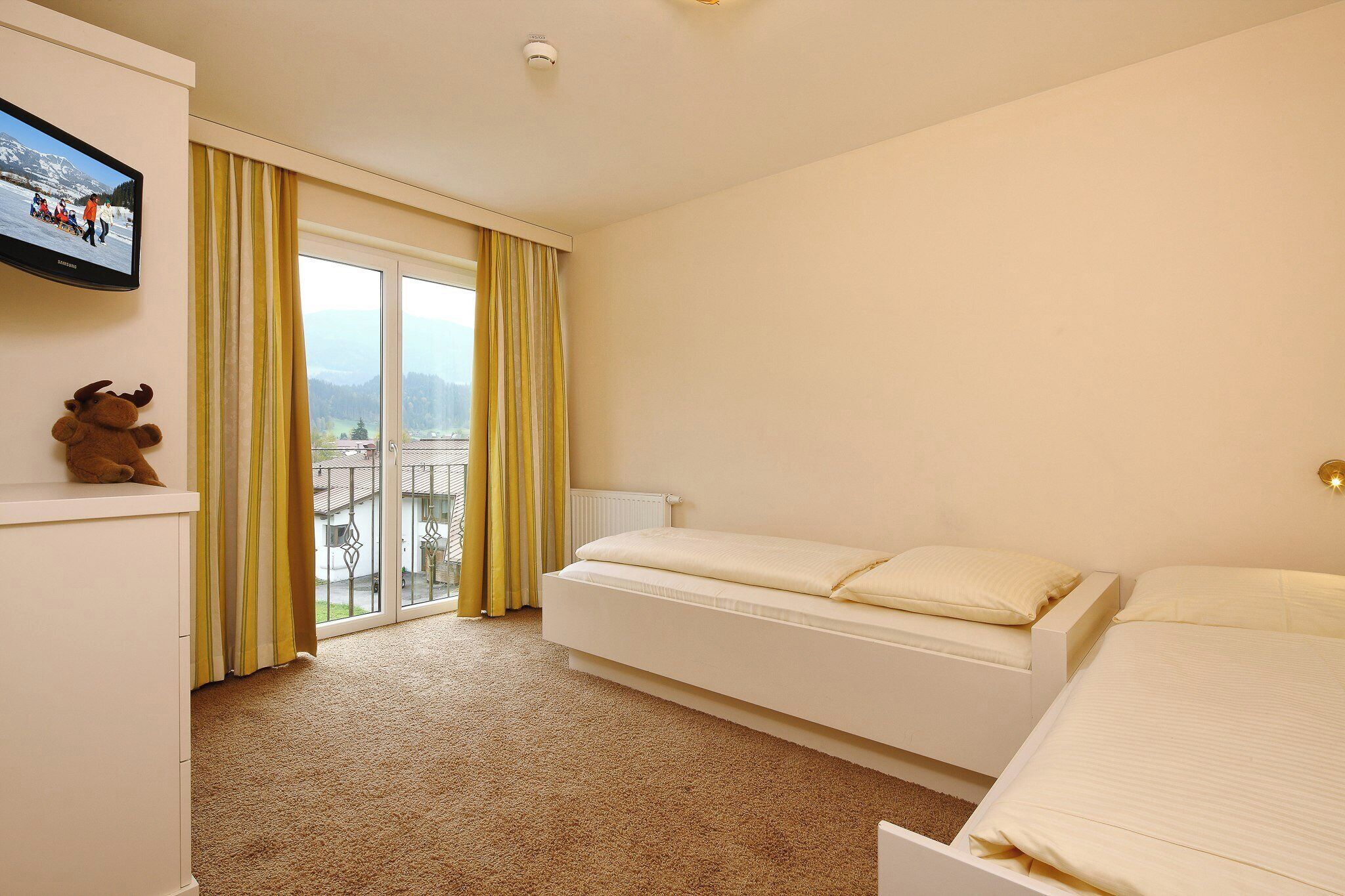 Hotelkamer met een bed, een slaapbank, een televisie, een raam met gordijnen en uitzicht op een besneeerd landschap.