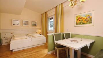 A hotel room with a bed, a table with a chair, a window with curtains, and wall art.