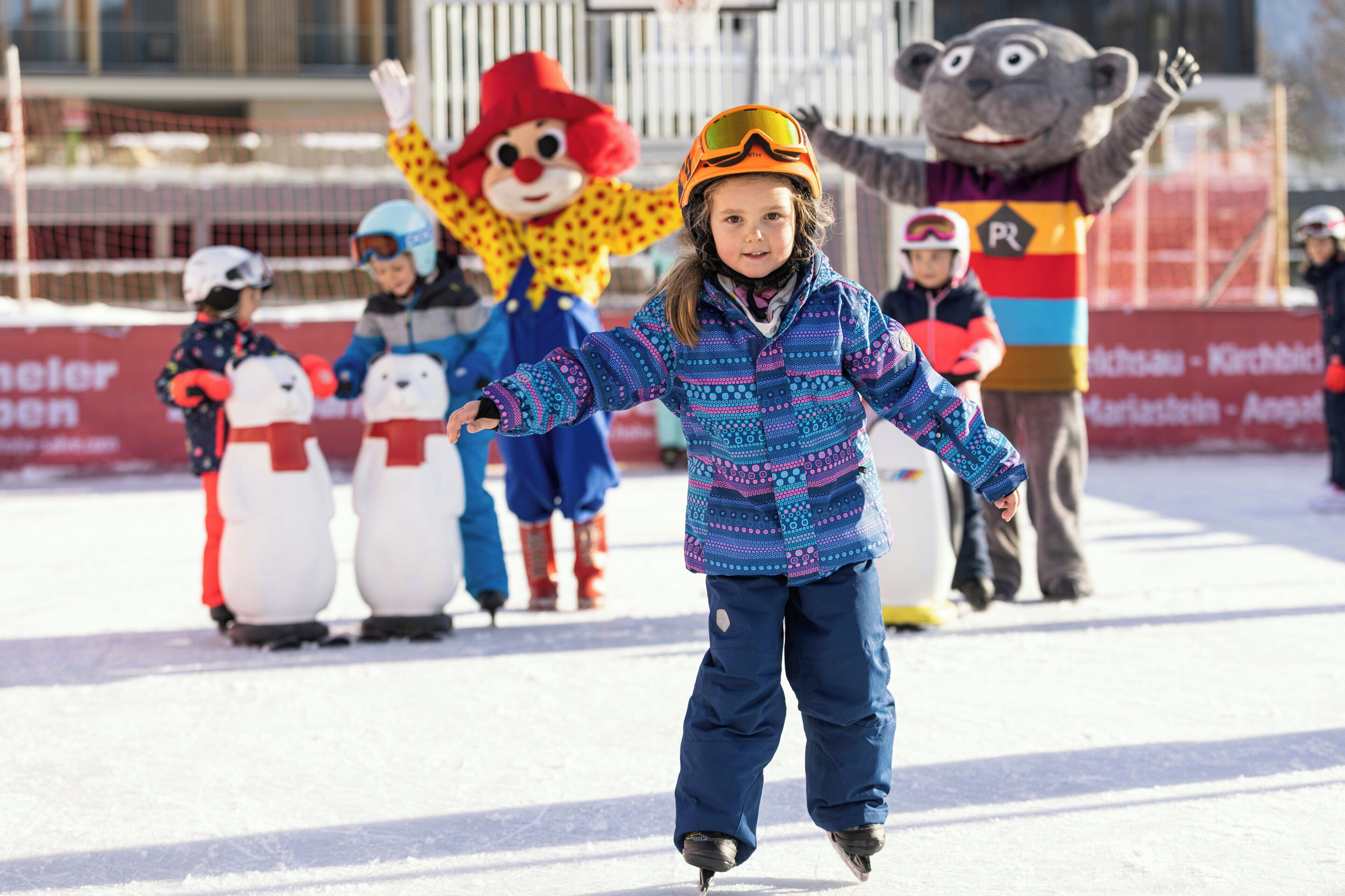 A child ice skating with a mascot and snowmen in the background.