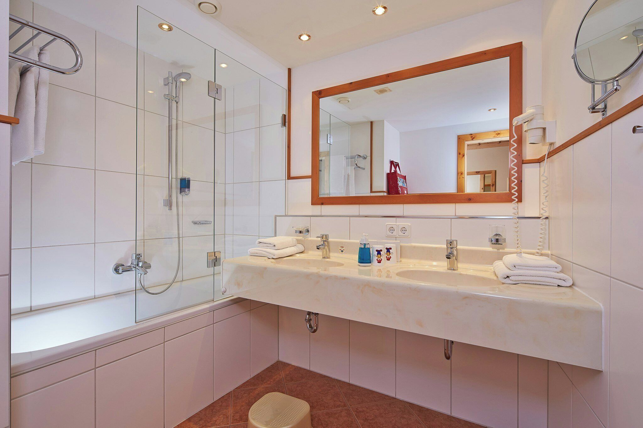 A modern bathroom with a glass shower enclosure, a double sink vanity, a large mirror, and a towel rack.