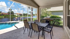 A covered outdoor area with a pool, a table with chairs, and a grill.