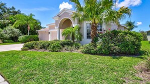 A two-story house with a central archway, surrounded by well-maintained lawns and palm trees.