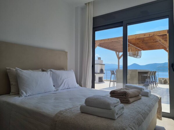 Un dormitorio con una cama grande, vista al mar y un patio con mesa y sillas.