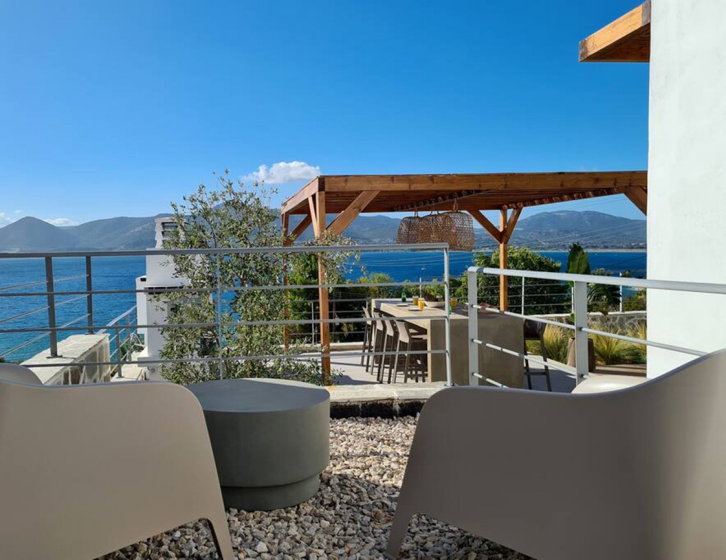 Une terrasse avec vue sur la mer, une pergola en bois et des sièges d’extérieur.