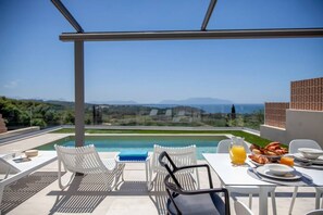 Une terrasse sur le toit avec une piscine, des chaises longues blanches et une table dressée pour le petit-déjeuner, avec des croissants et du jus d’orange.