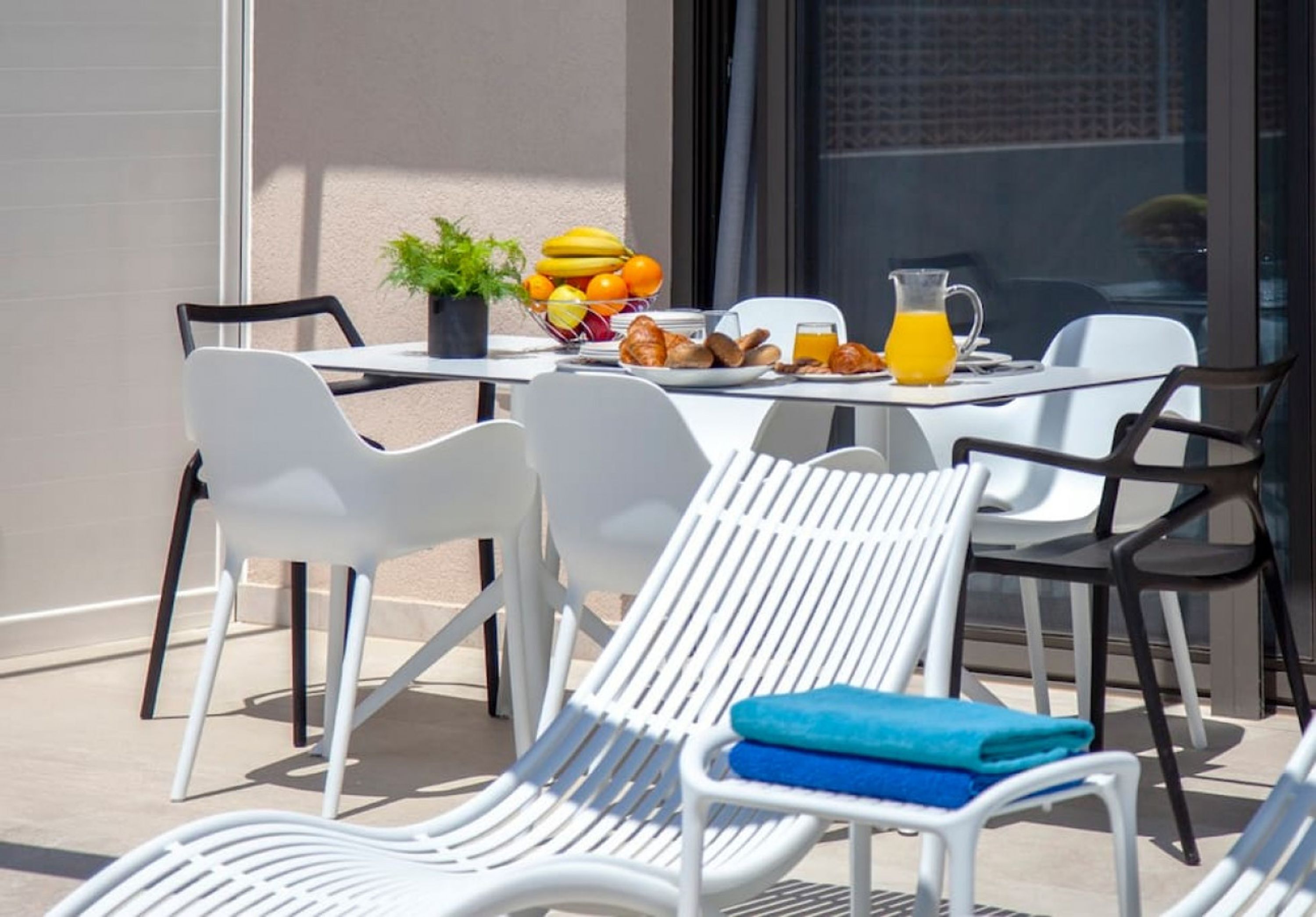 An outdoor dining area with white chairs and a table set for breakfast.