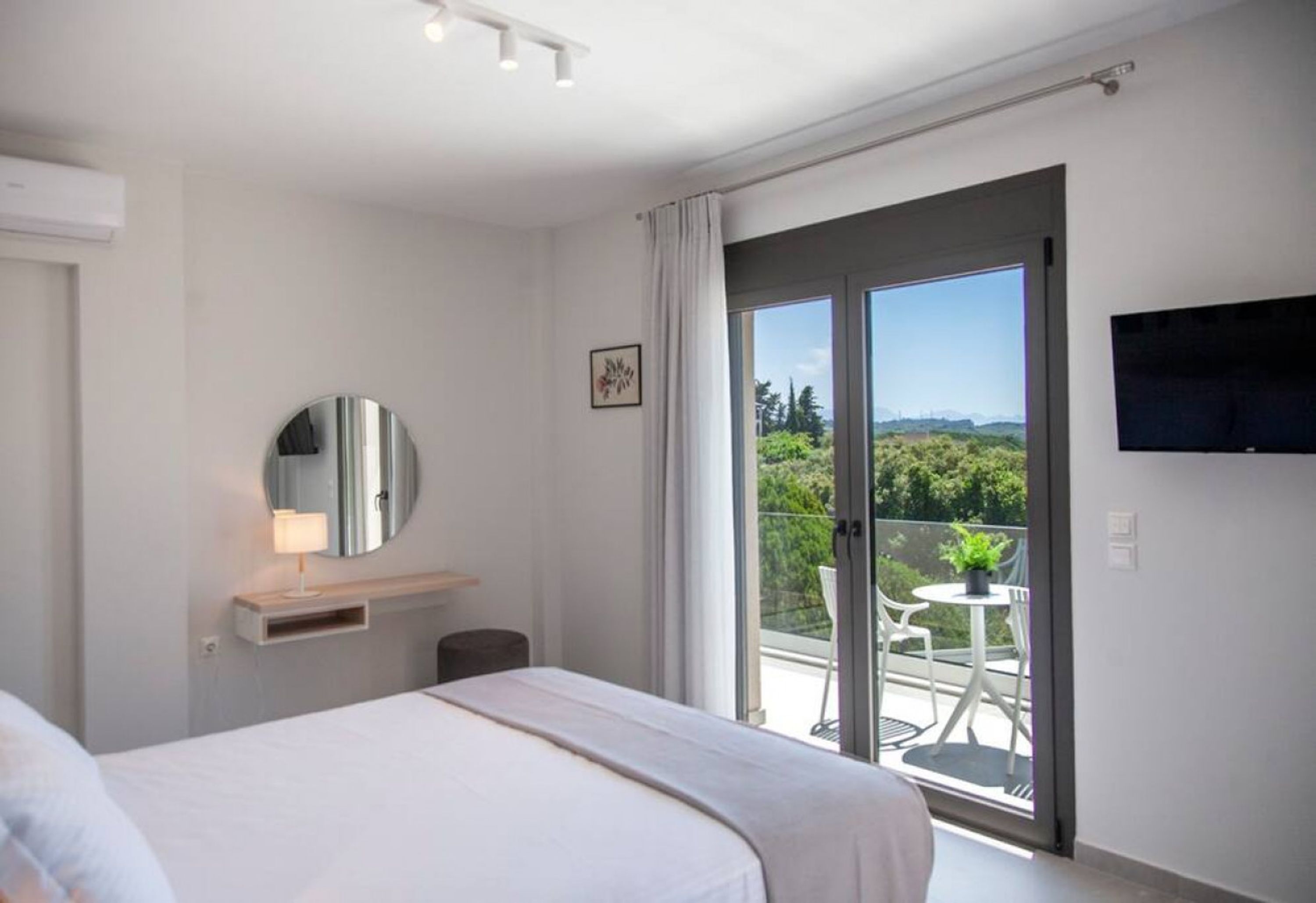Une chambre d’hôtel comprenant un lit, une table de chevet avec une lampe, un miroir, un téléviseur fixé au mur et un balcon avec une table et des chaises.