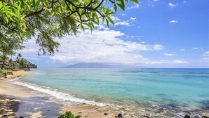 A beach with clear turquoise water, a sandy shore, and a view of a distant mountain range. - Kuleana 405 Oceanfront 1Bedroom 1 Condo by RedAwning (Lahaina)