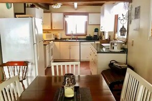 Una cocina compacta con muebles blancos, un refrigerador y una mesa de comedor con sillas.