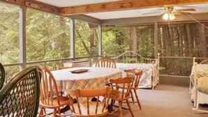 Un'area pranzo esterna riparata con tavolo e sedie, circondata da pareti di vetro e vista sulla foresta.