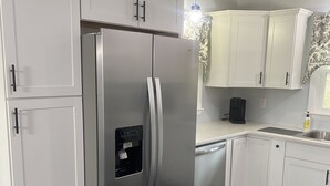 A modern kitchen with white cabinets, a stainless steel refrigerator, and dark tiled flooring.