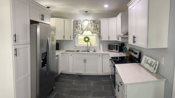 A modern kitchen with white cabinets, a stainless steel refrigerator, a microwave, and a stone tile floor.