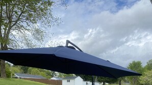 A patio with wicker furniture, a large umbrella, and a patterned rug.