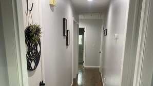 A hallway with wooden flooring, white walls, and a door with a black decorative piece.