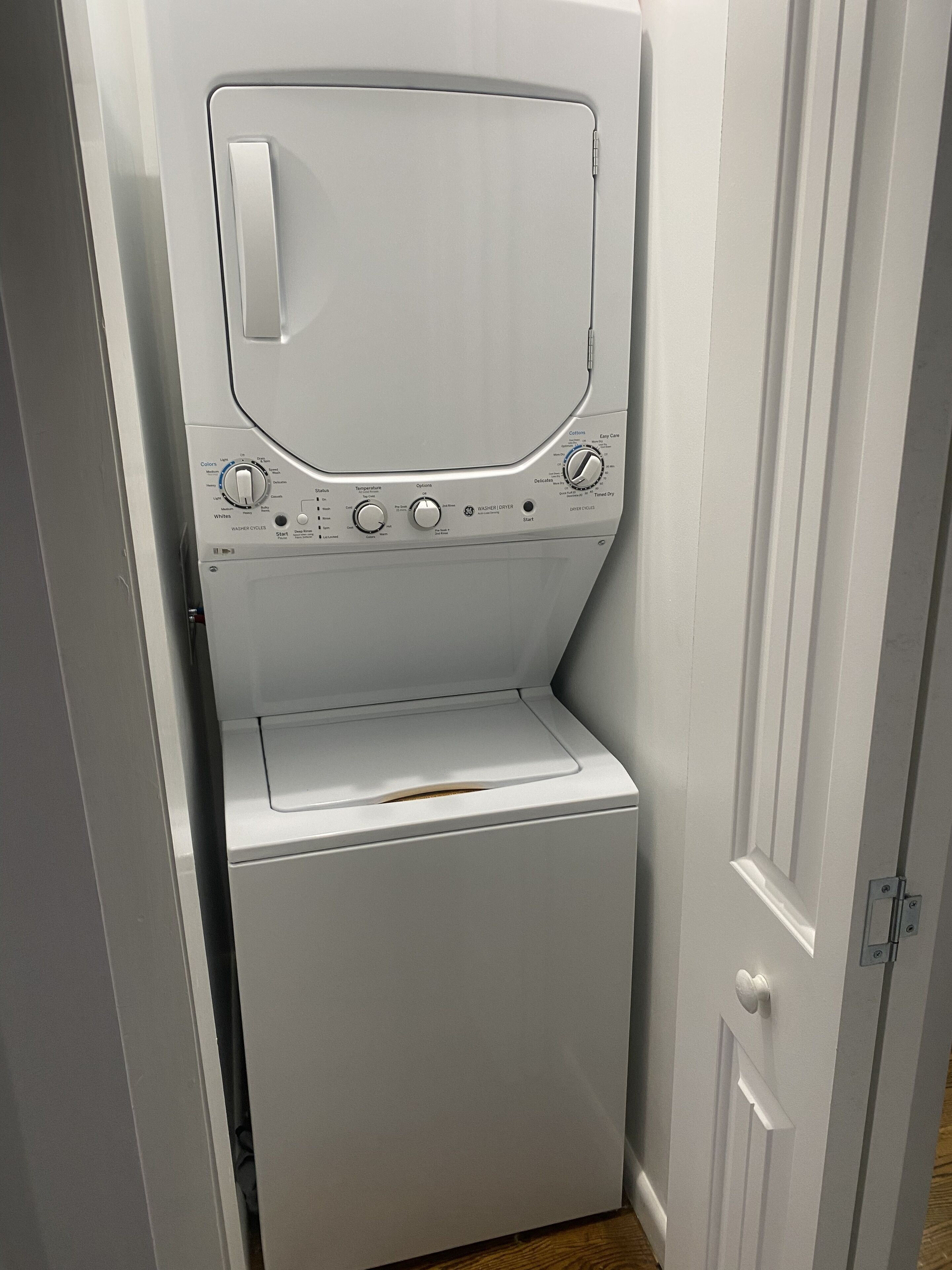 A compact, white front-loading washing machine in a narrow space, likely a utility room or laundry area.