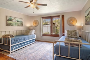 A room with two single beds, a ceiling fan, a large window with a view, and decorative wall art.